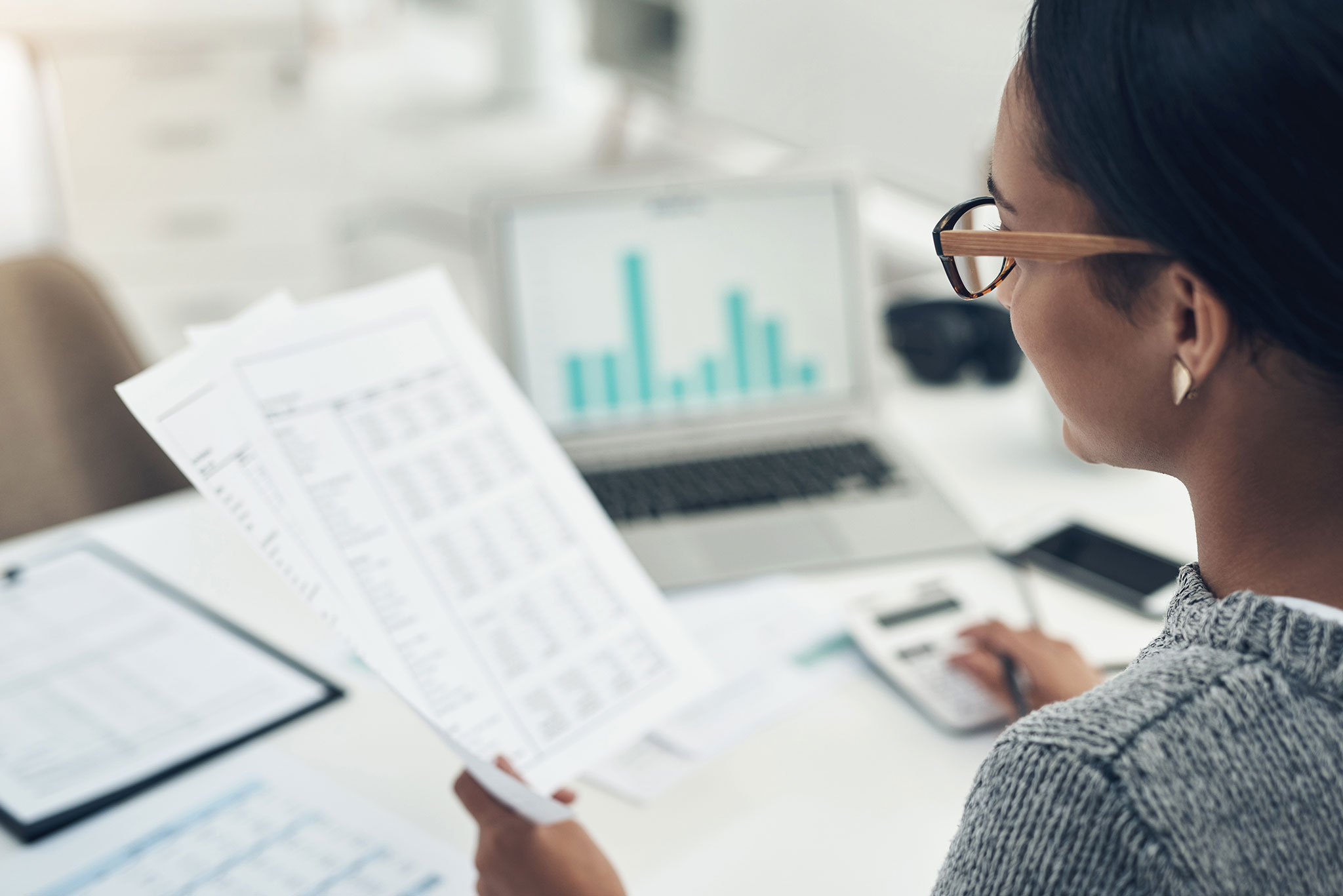 Woman reading a report next to a laptop showing a bar chart