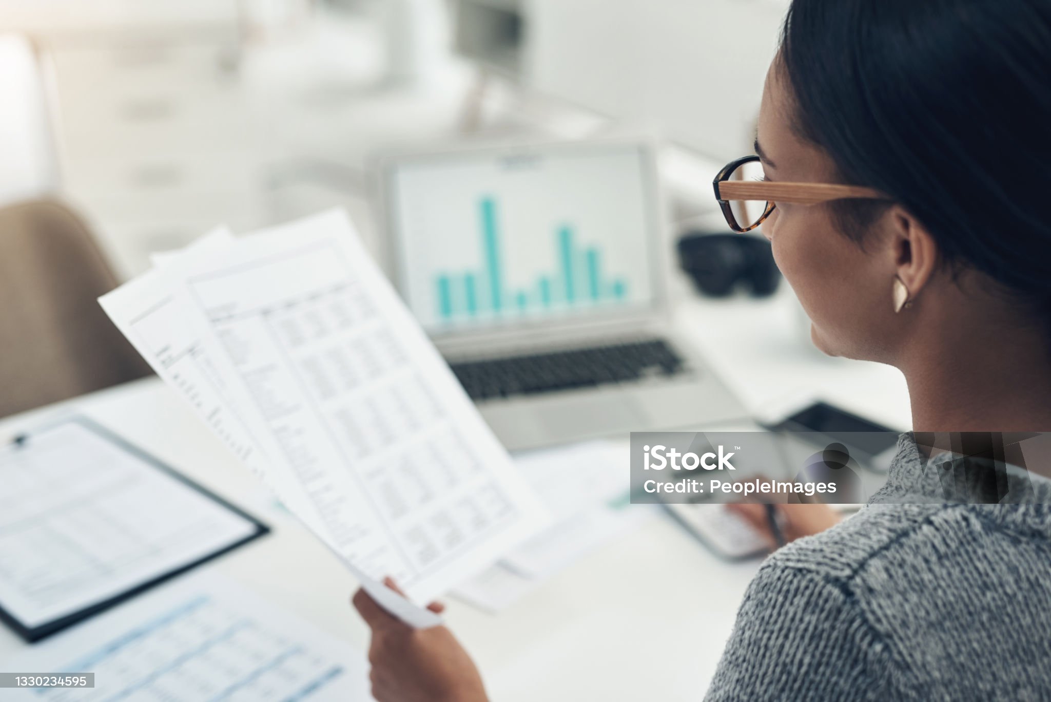Woman reading a report next to a laptop showing a bar chart