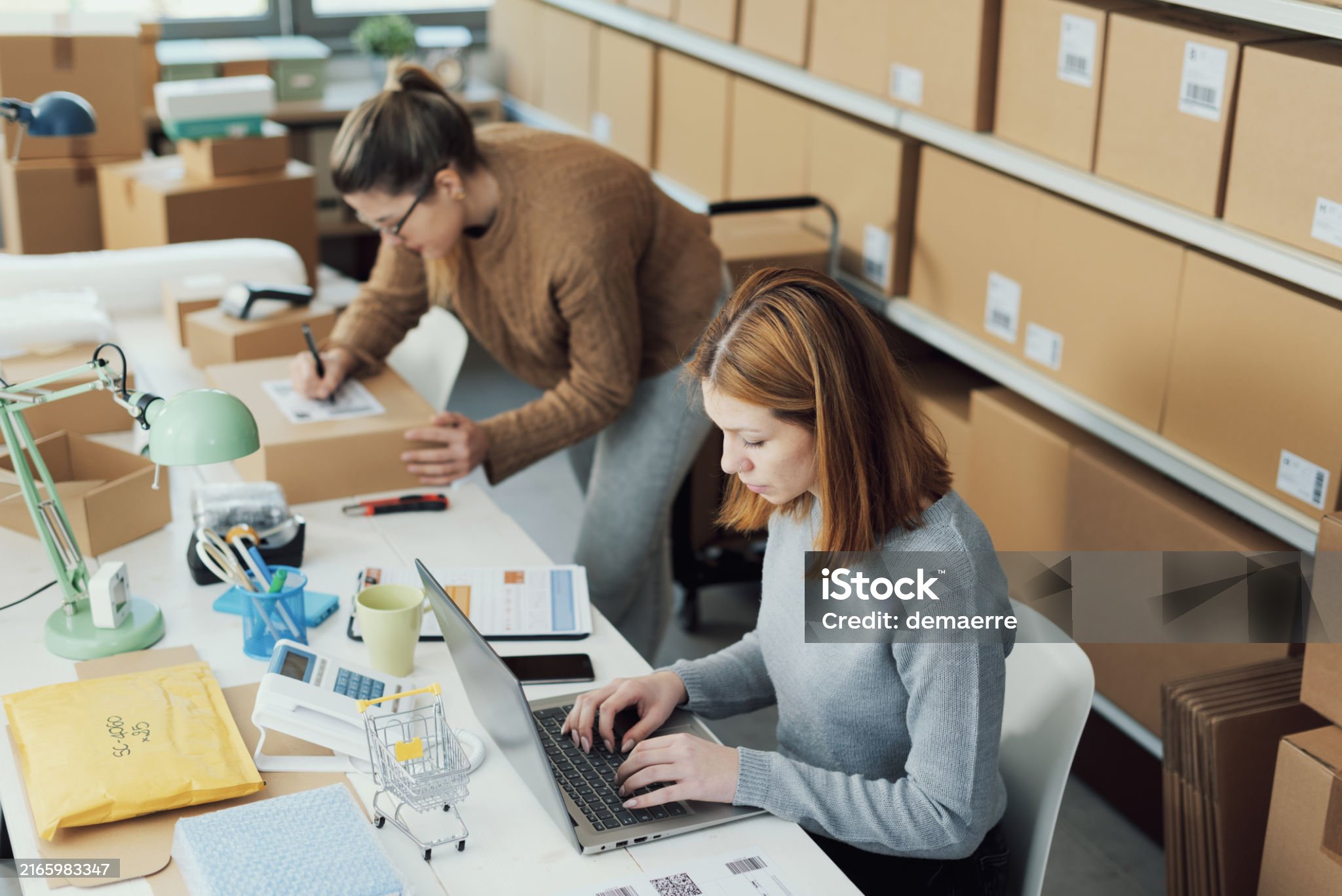 Women in warehouse working on computers near shelves of boxes
