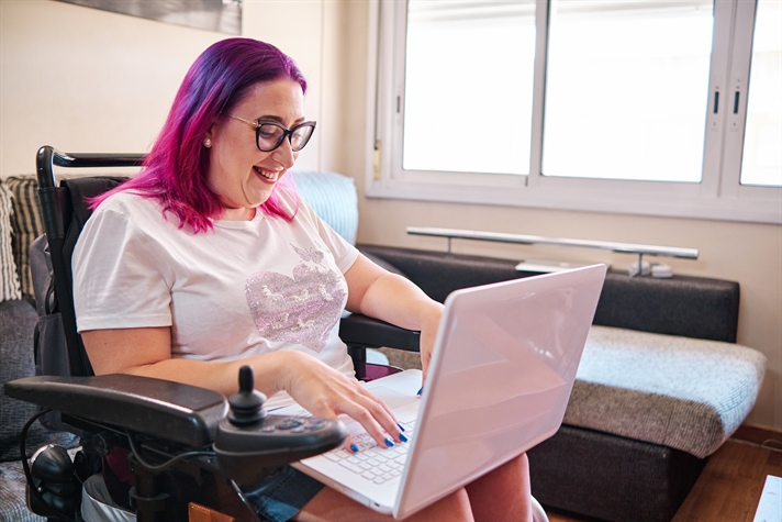 Adult woman with disabilities in a wheelchair working at home with laptop