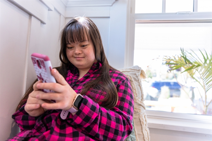Young woman with Downs Syndrome using her smartphone by the window