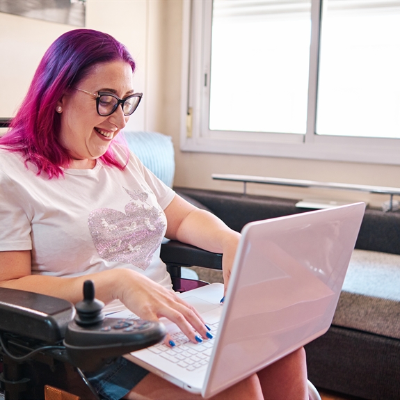 Adult woman with disabilities in a wheelchair working at home with laptop