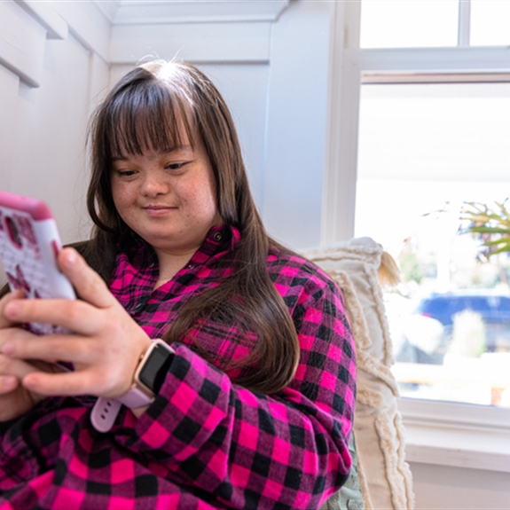 Young woman with Downs Syndrome using her smartphone by the window